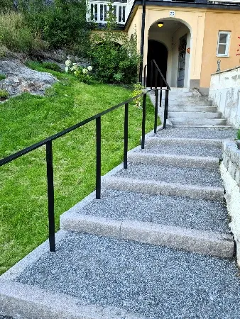 Ledstång längs en lång stentrappa upp mot ett hus