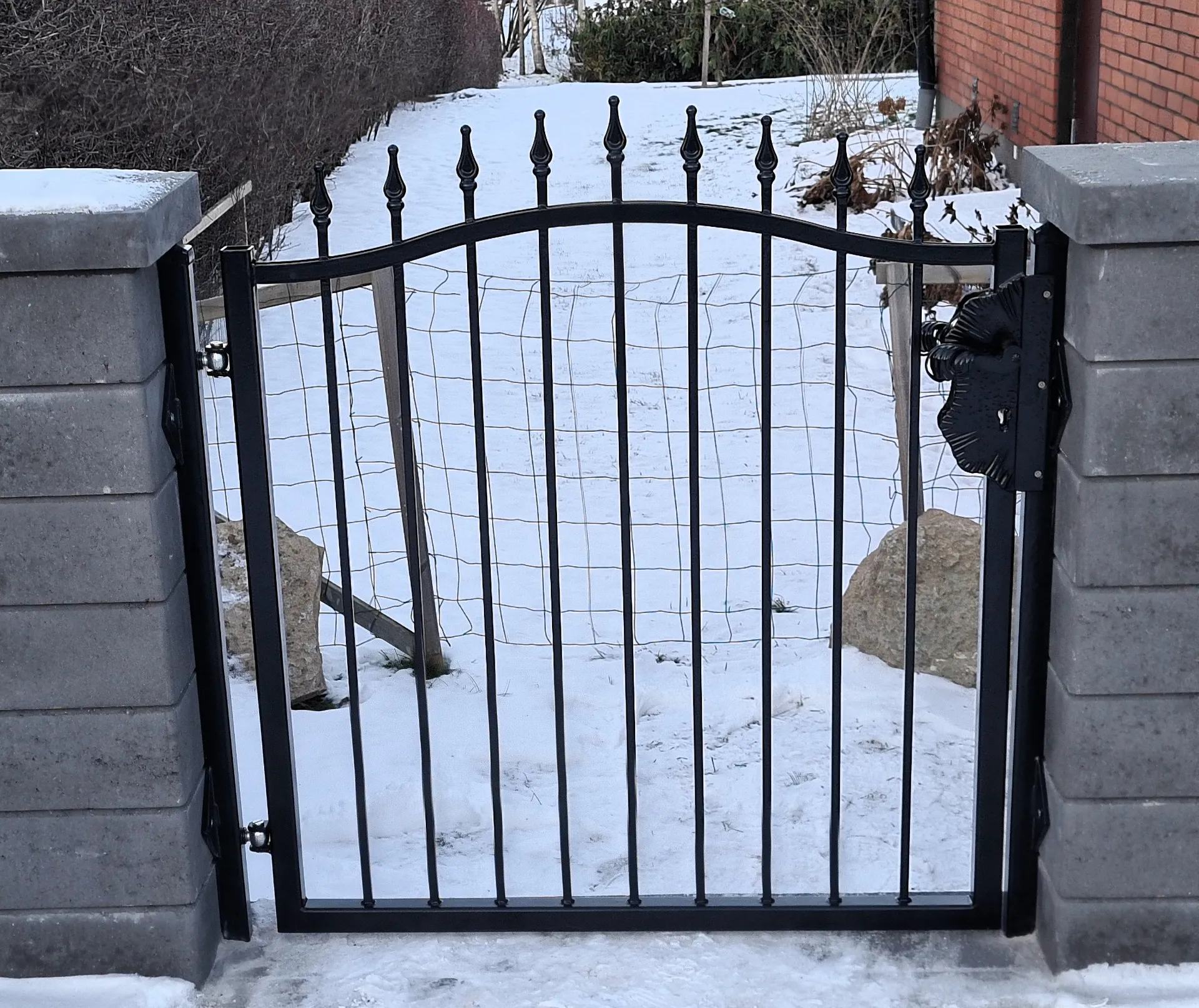 Svart smidesgrind mellan två stenpelare i snön
